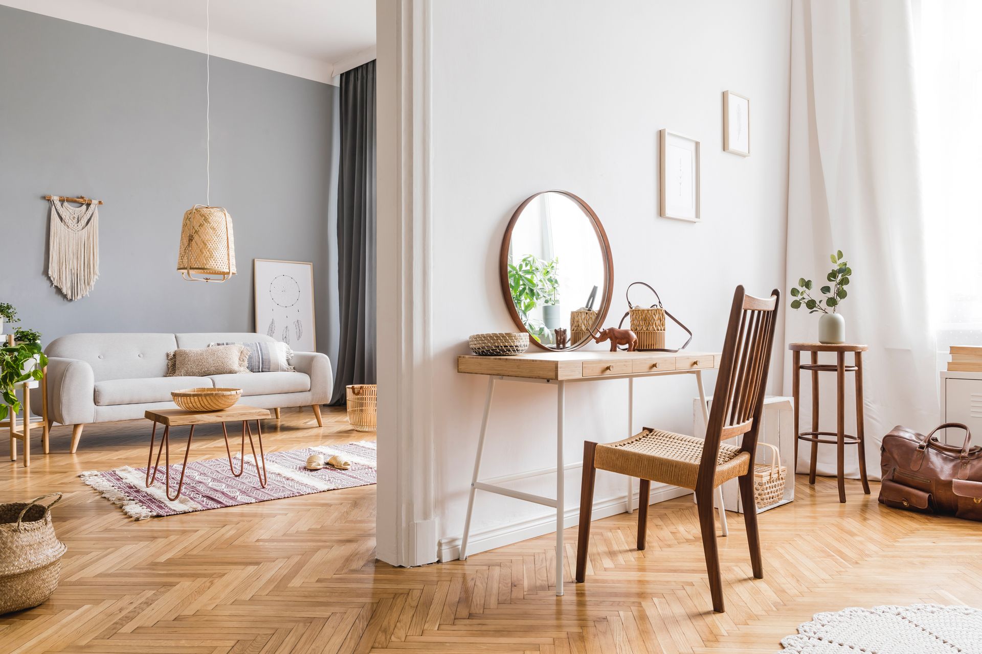 Bright living room with a desk, round mirror, chair, sofa, rug, and wood floors in soft neutral tones