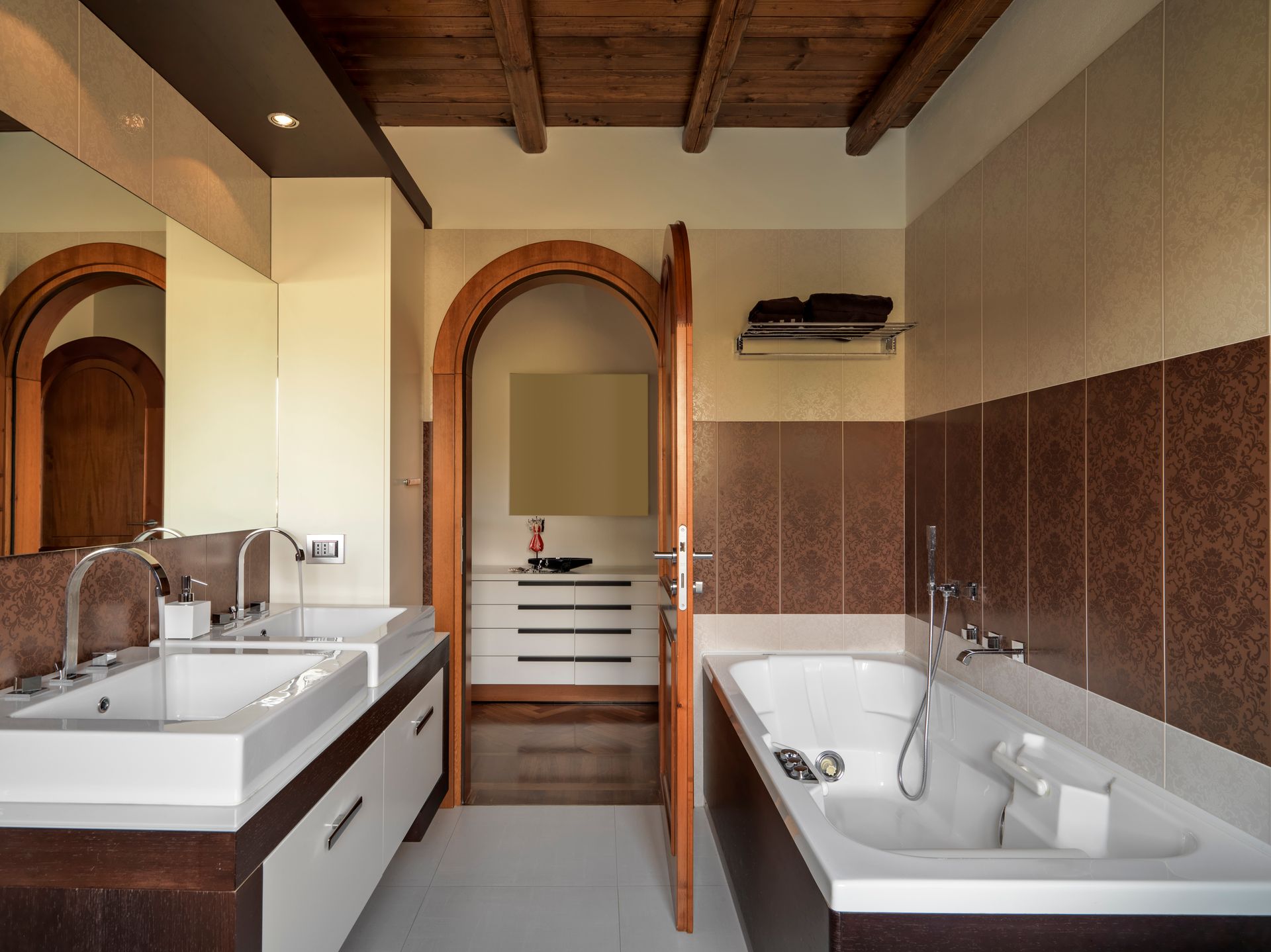 Modern bathroom with double sink vanity, arched doorway, and tiled bathtub