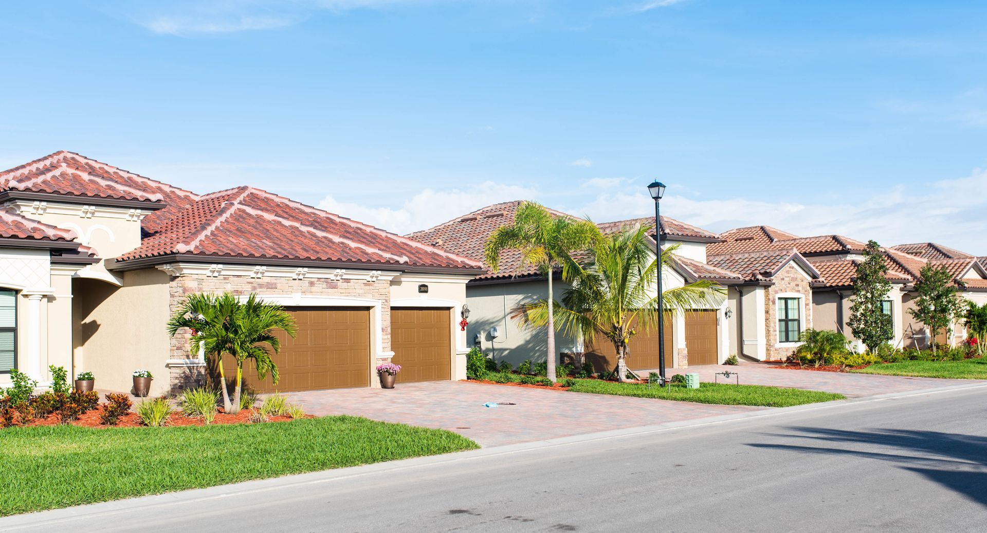 Suburban street with beige houses, red tile roofs, palm trees, and a clear blue sky