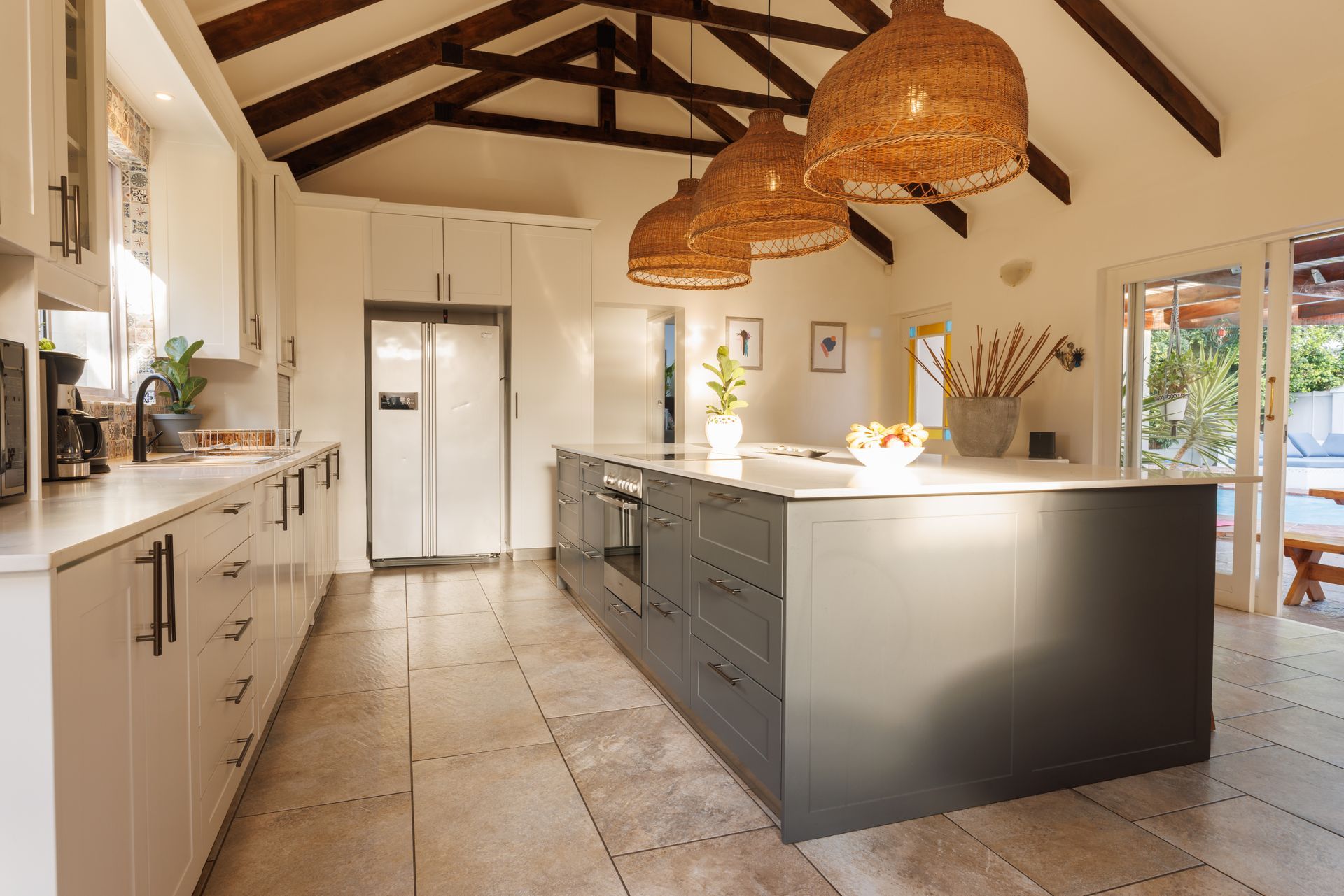 Spacious modern kitchen with white walls, gray island, wood beams, and woven pendant lights