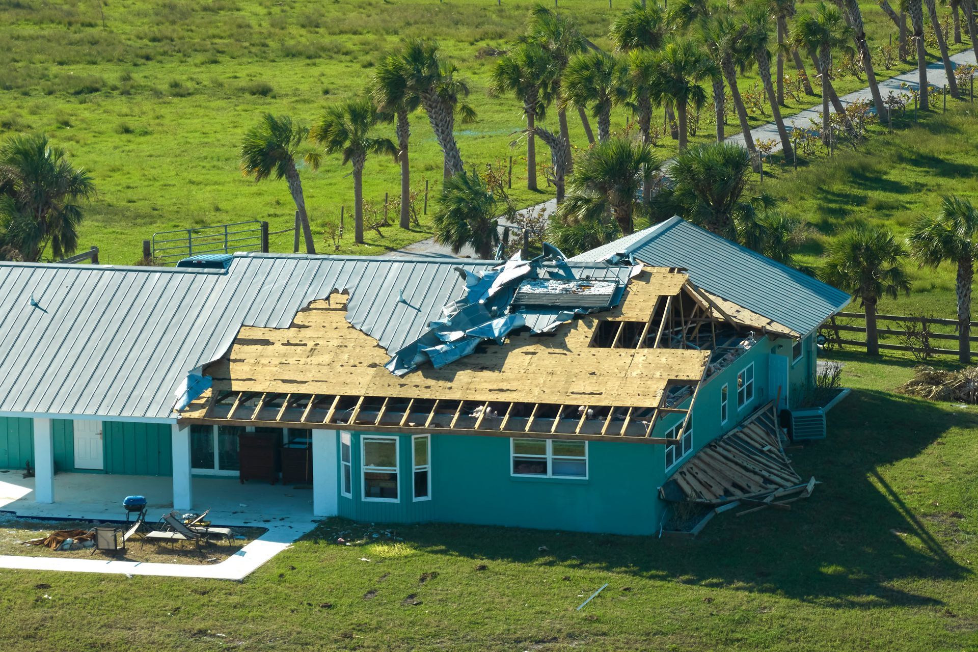 Damaged turquoise house roof with scattered debris in a green rural field
