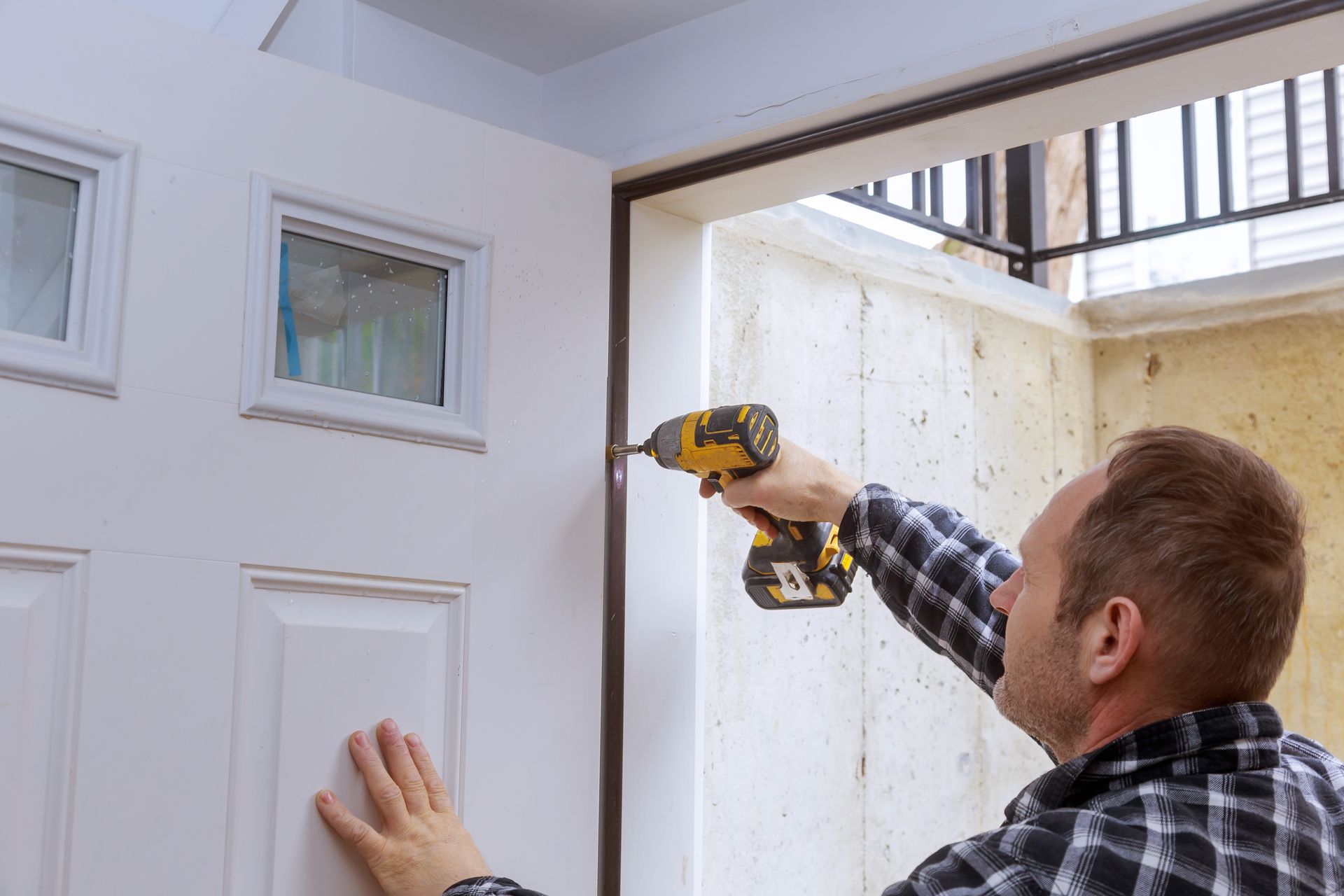 Person using a drill to install a door hinge on a white exterior door frame