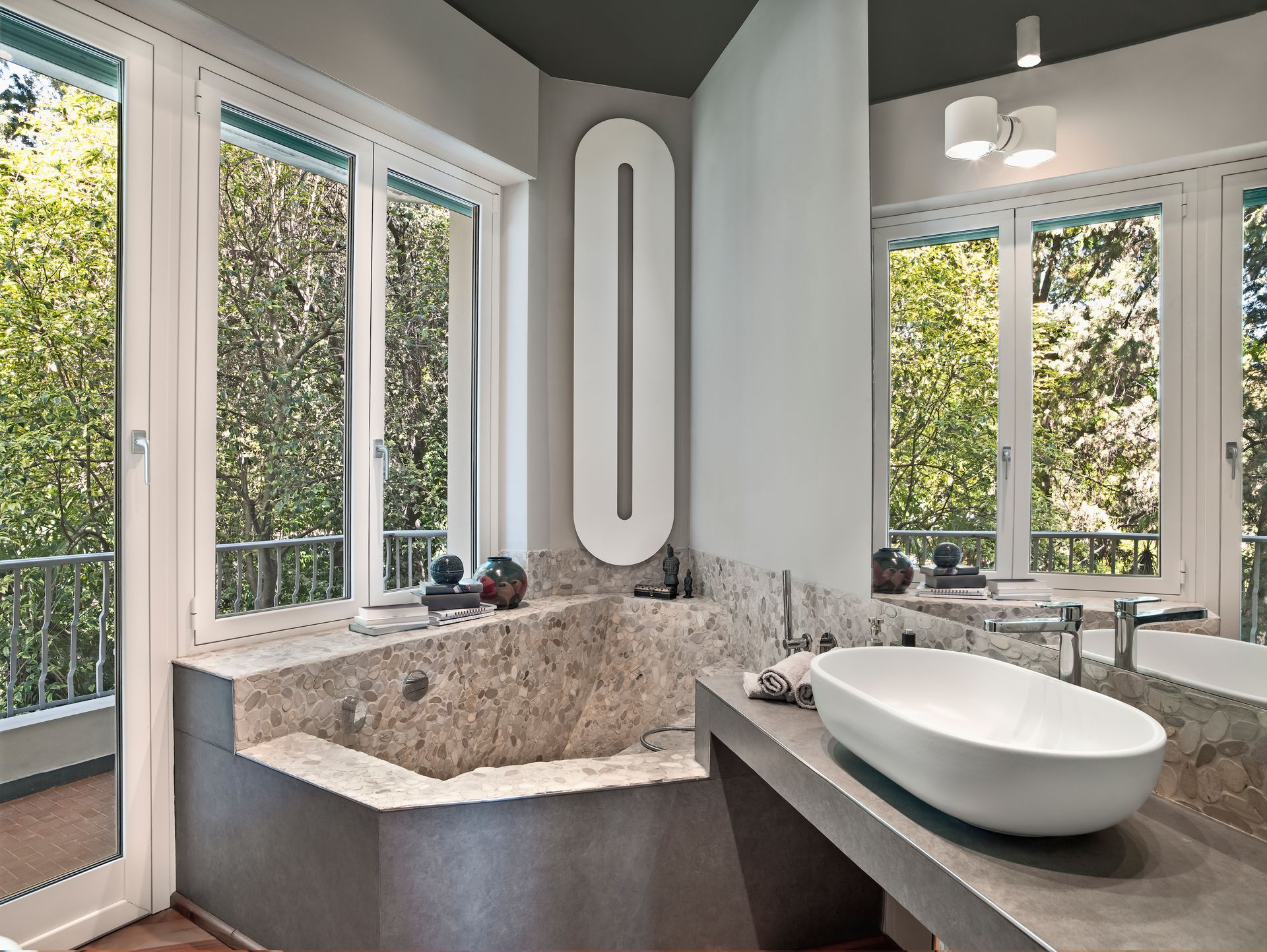 Modern bathroom with double windows, stone soaking tub, and white vessel sink