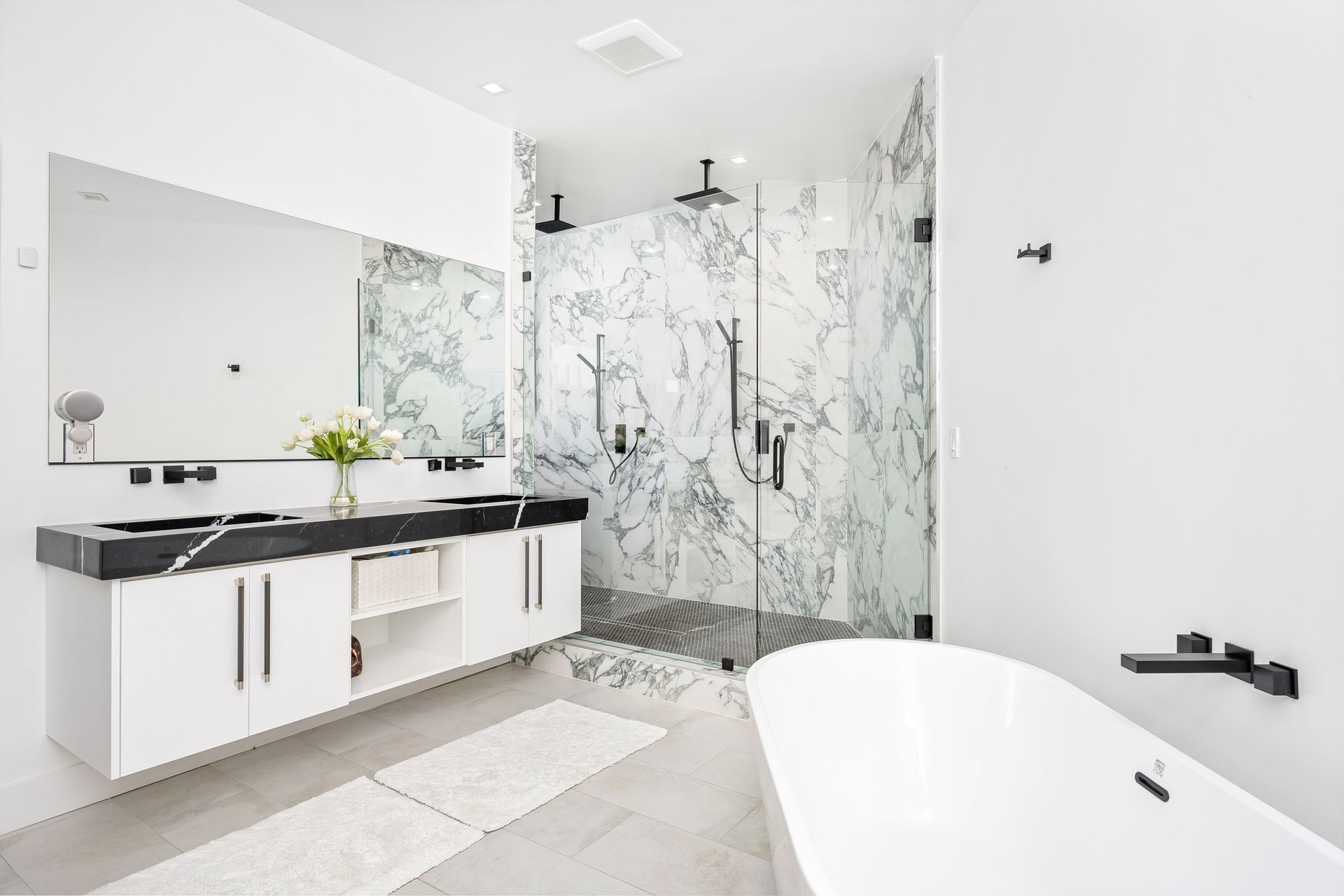 Modern white bathroom with large mirror, double vanity, glass shower, and freestanding tub
