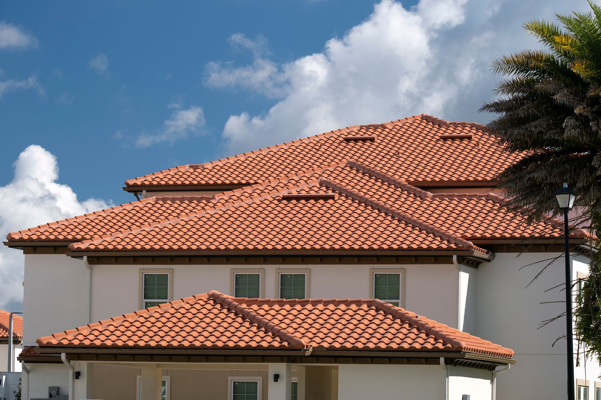 Two-story house with red tile roof under a blue sky with clouds