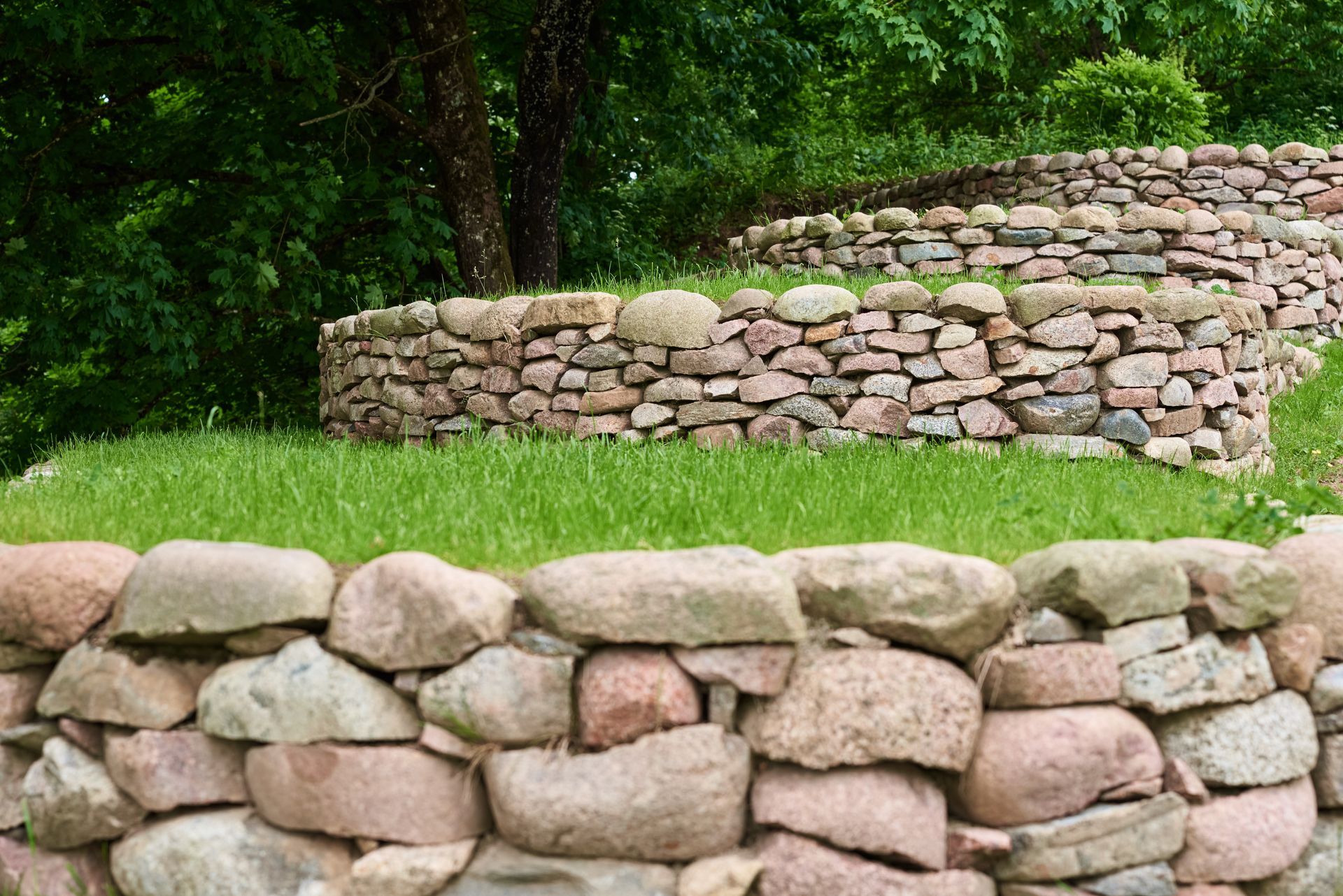 Stone retaining walls terracing a grassy hillside with green trees in the background