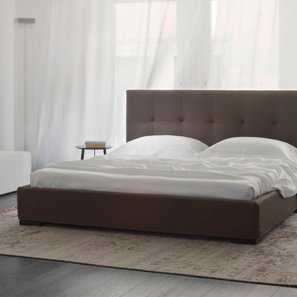 Un dormitorio con una cama marrón y sábanas blancas