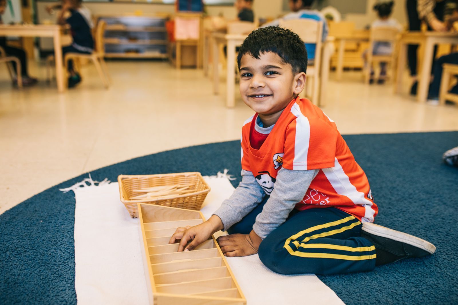 A young boy is sitting on the floor in a classroom playing with wooden blocks.