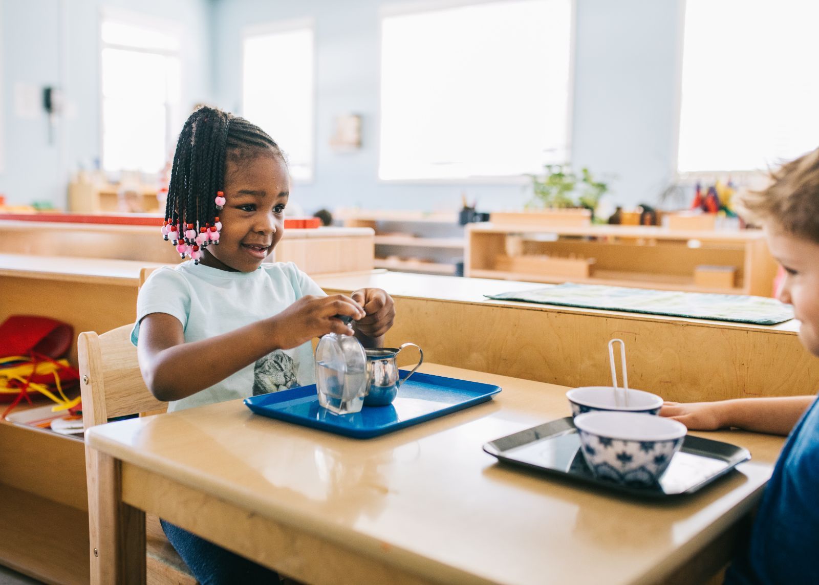 A boy and a girl are sitting at a table playing with a tea set.
