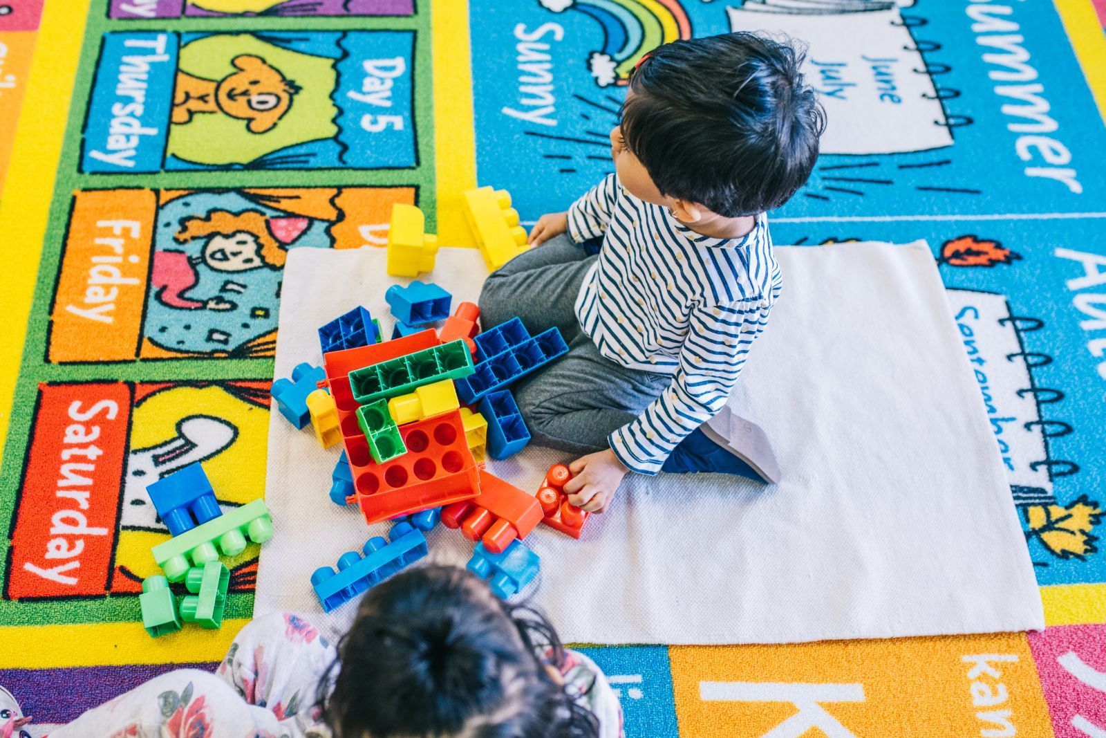 A boy and a girl are playing with blocks on a rug.