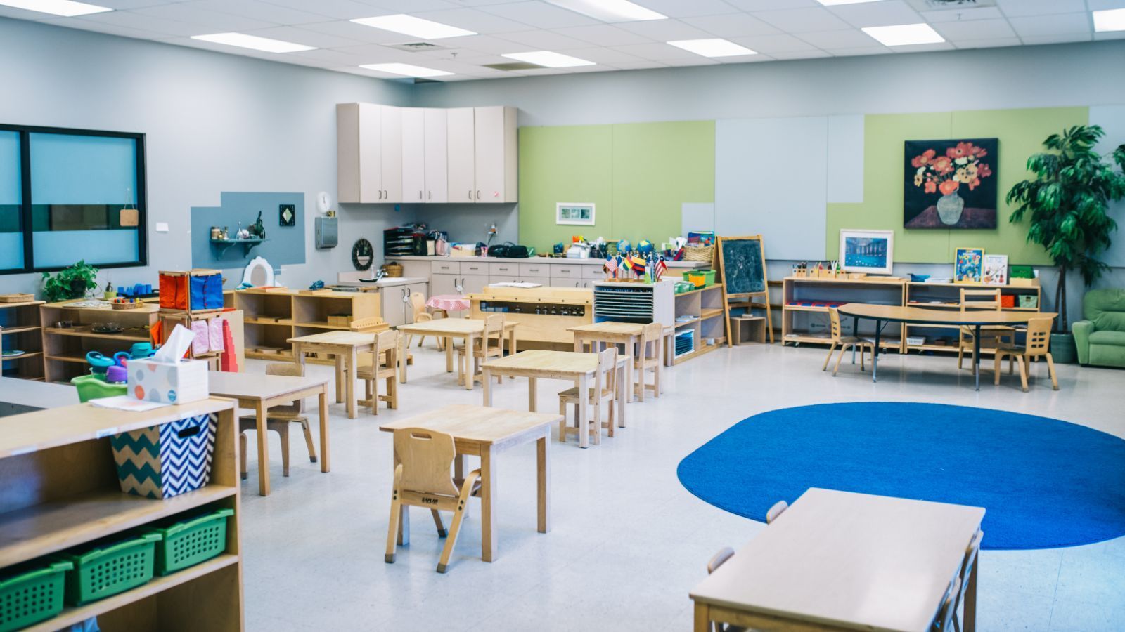 A classroom with tables and chairs and a blue rug.