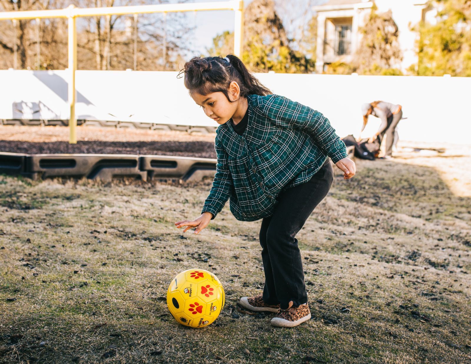 A little girl is kicking a yellow soccer ball in a field.