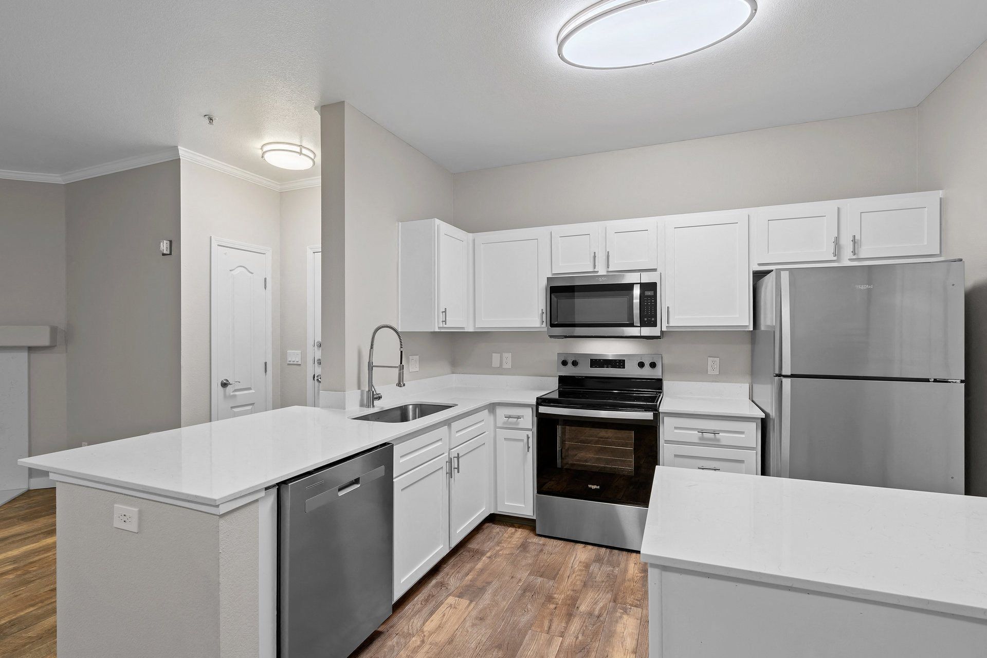 White kitchen with stainless steel fridge, oven, microwave, and an island with sink.