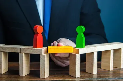 A man holding a block creating a bridge between two parties in litigation represented by building blocks shaped like people