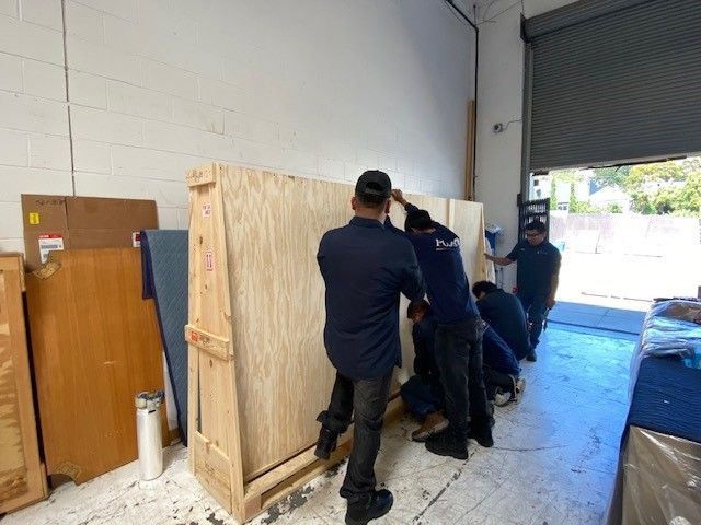 A group of men are moving a large wooden box in a warehouse.