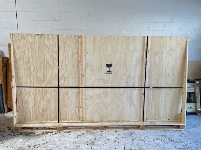 A large wooden crate is sitting on top of a pallet in a room. Secure transportation of custom crating.