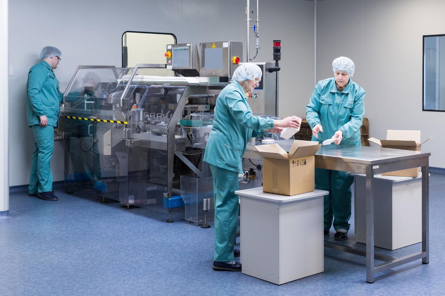 Workers in teal lab uniforms packaging items in a clean factory room