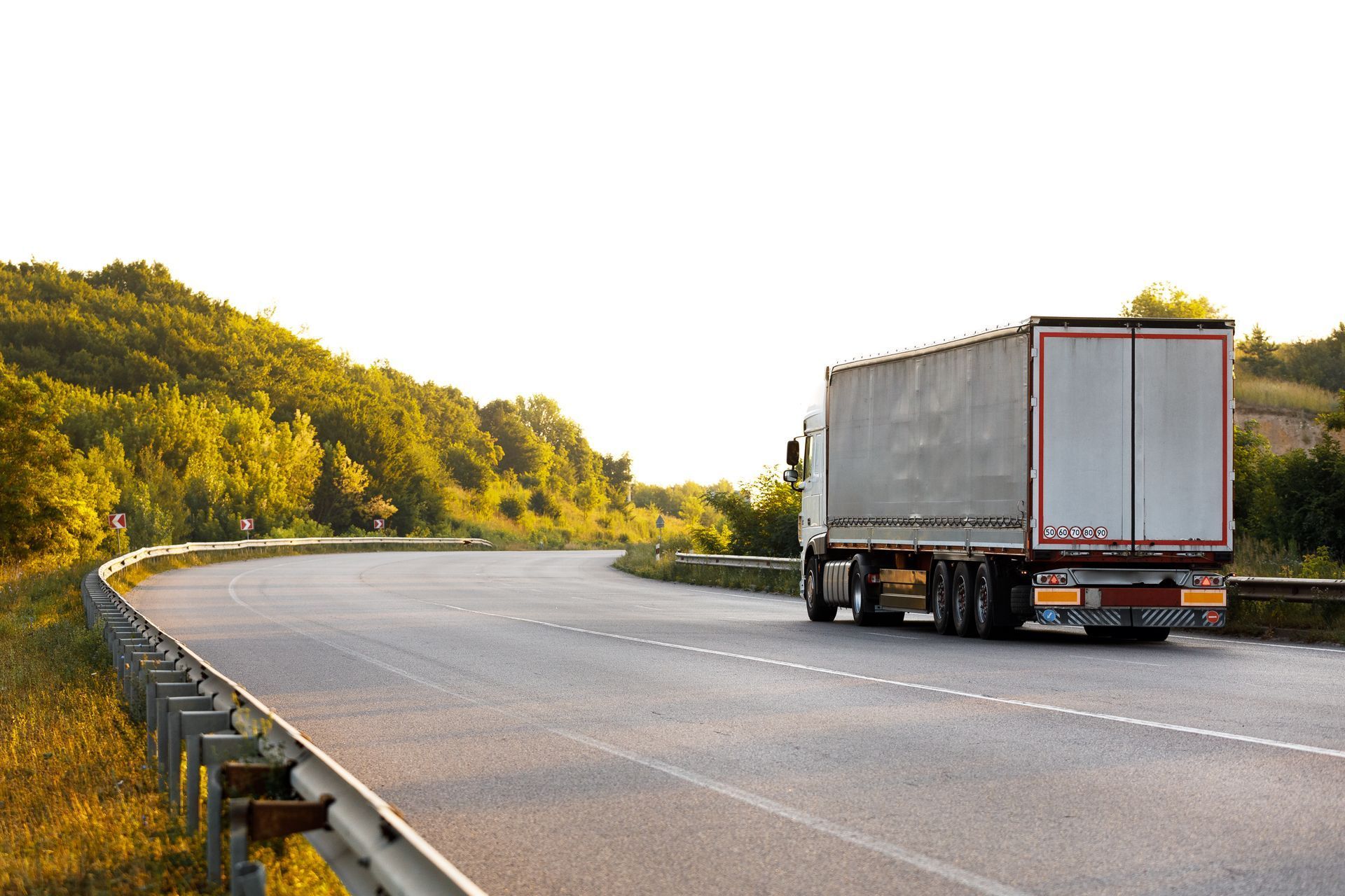 A white semi truck is driving down a curvy highway. Secure and smooth long distance movers.