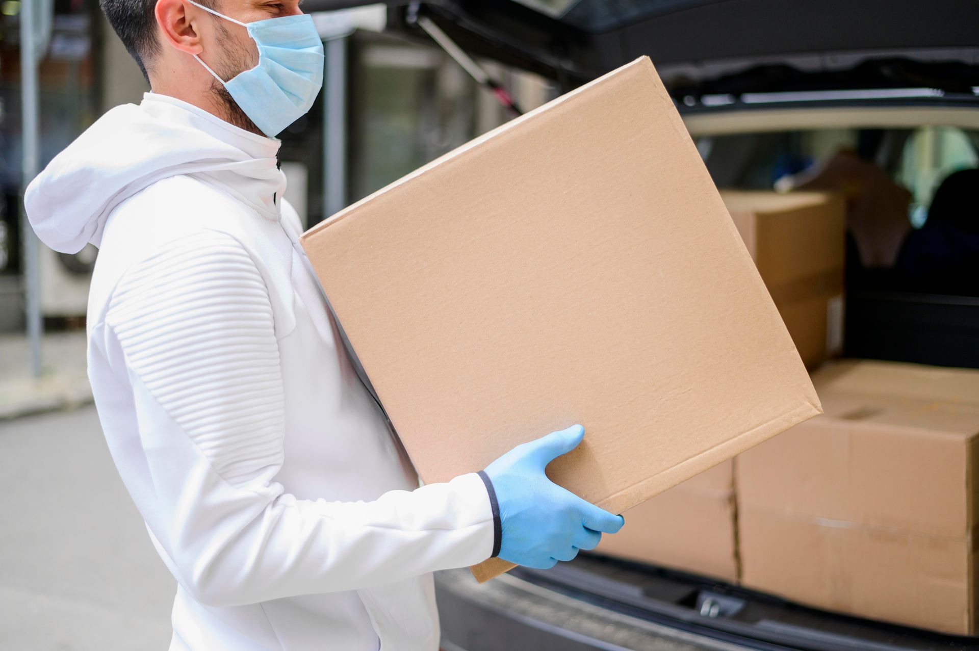 A man wearing a mask and gloves is carrying a cardboard box. Cost-effective lab equipment transportation.