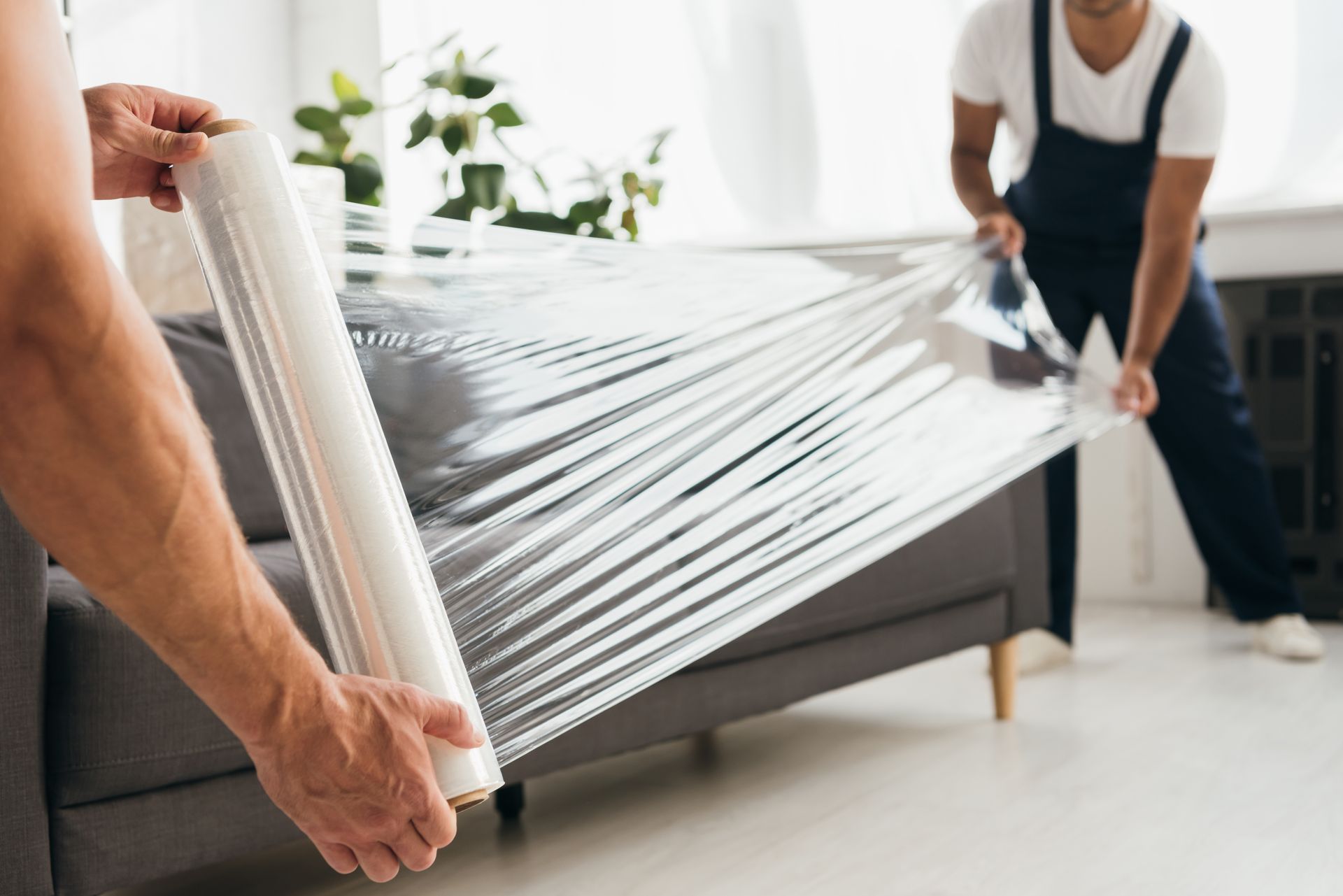 A man is holding a roll of plastic wrap in front of a couch. Stress-free, secure home movers.