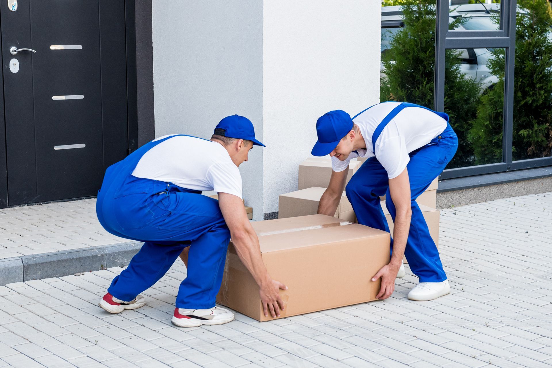 Two men are lifting a cardboard box on a sidewalk. Expert packing and relocation services.