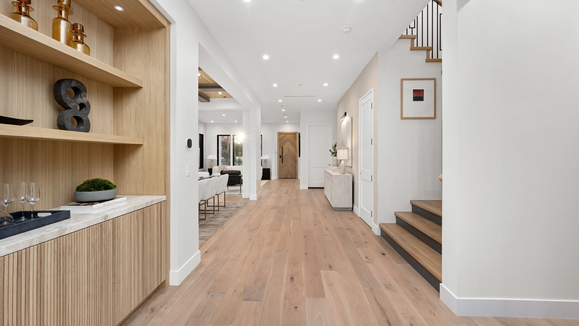 Une entrée de maison moderne avec un parquet clair, une étagère intégrée et un escalier en bois menant à l'étage.