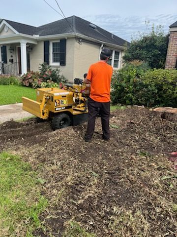 A man is working on a stump grinder in front of a house.