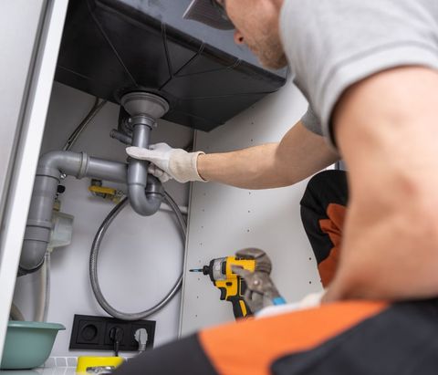 A man is fixing a sink with a drill.