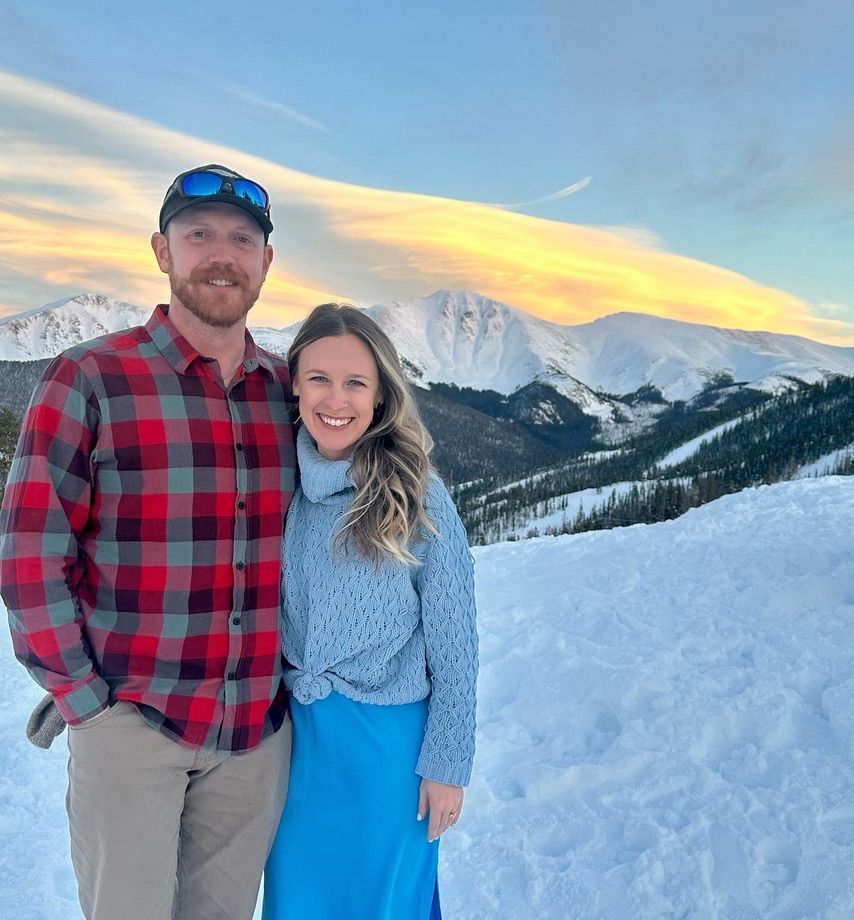 a man and women posing in front of a snow capped mountain