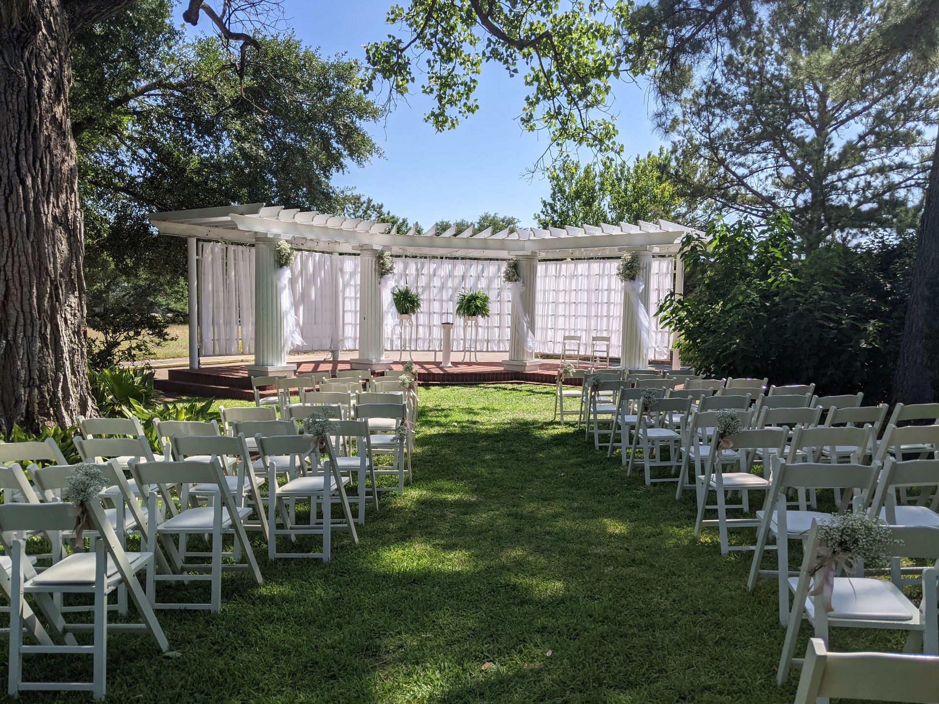 A row of white folding chairs are lined up in a grassy field.