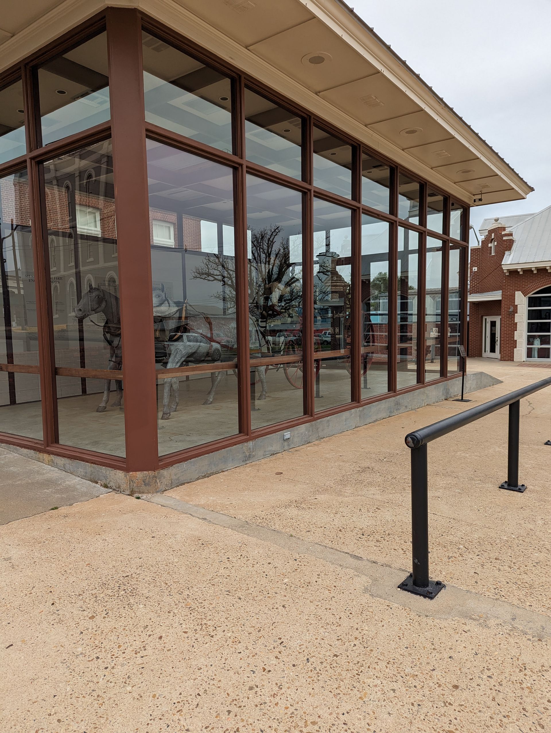 A glass-enclosed display case stands on a gravel patio, housing a vintage stagecoach pulled by statues of horses.