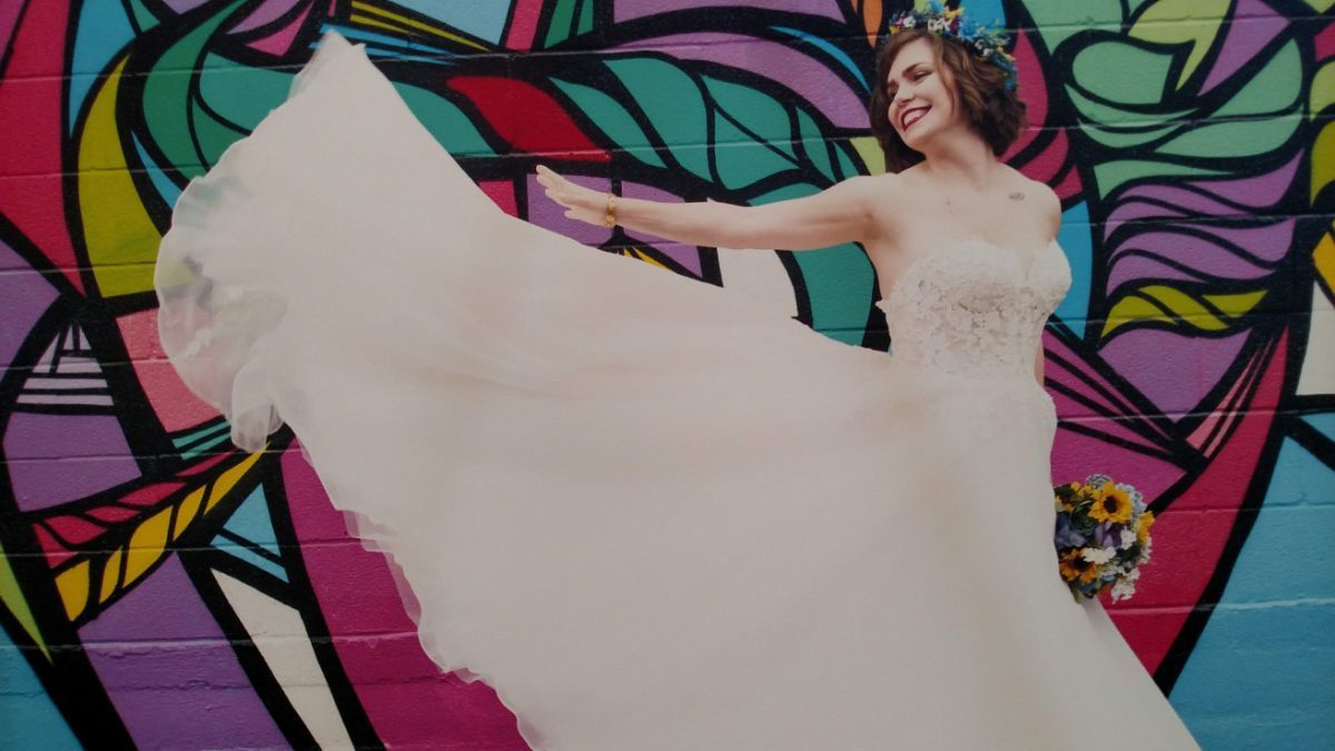 A bride in a wedding dress is standing in front of a colorful graffiti wall.