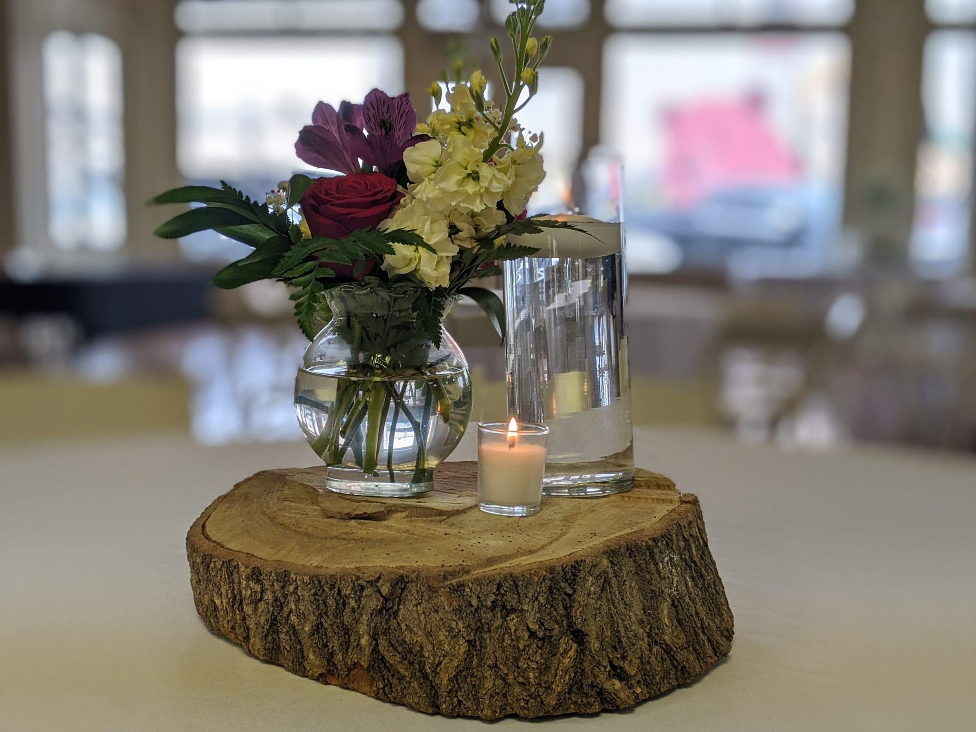 A wooden stump with a vase of flowers and a candle on it.