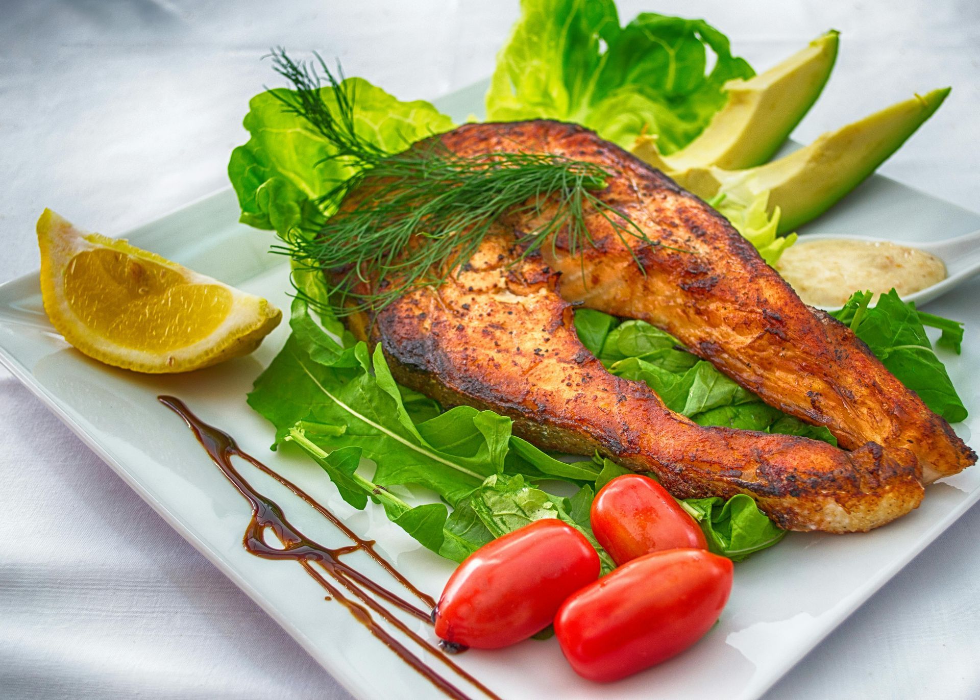 A white plate topped with a piece of salmon avocado and tomatoes