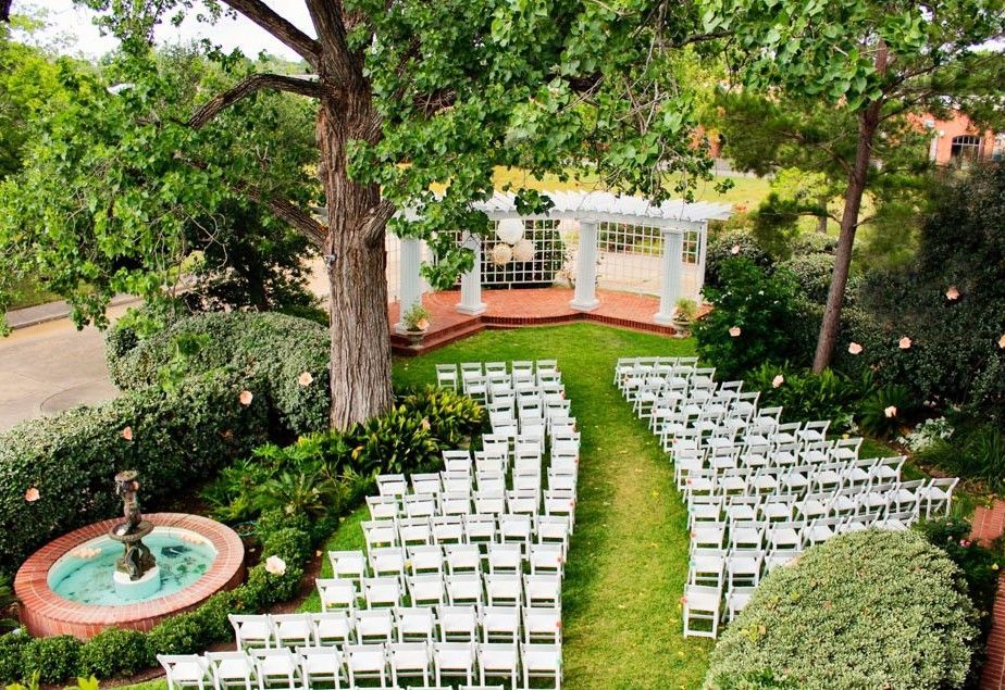A row of white chairs are lined up in a garden in front of a gazebo.