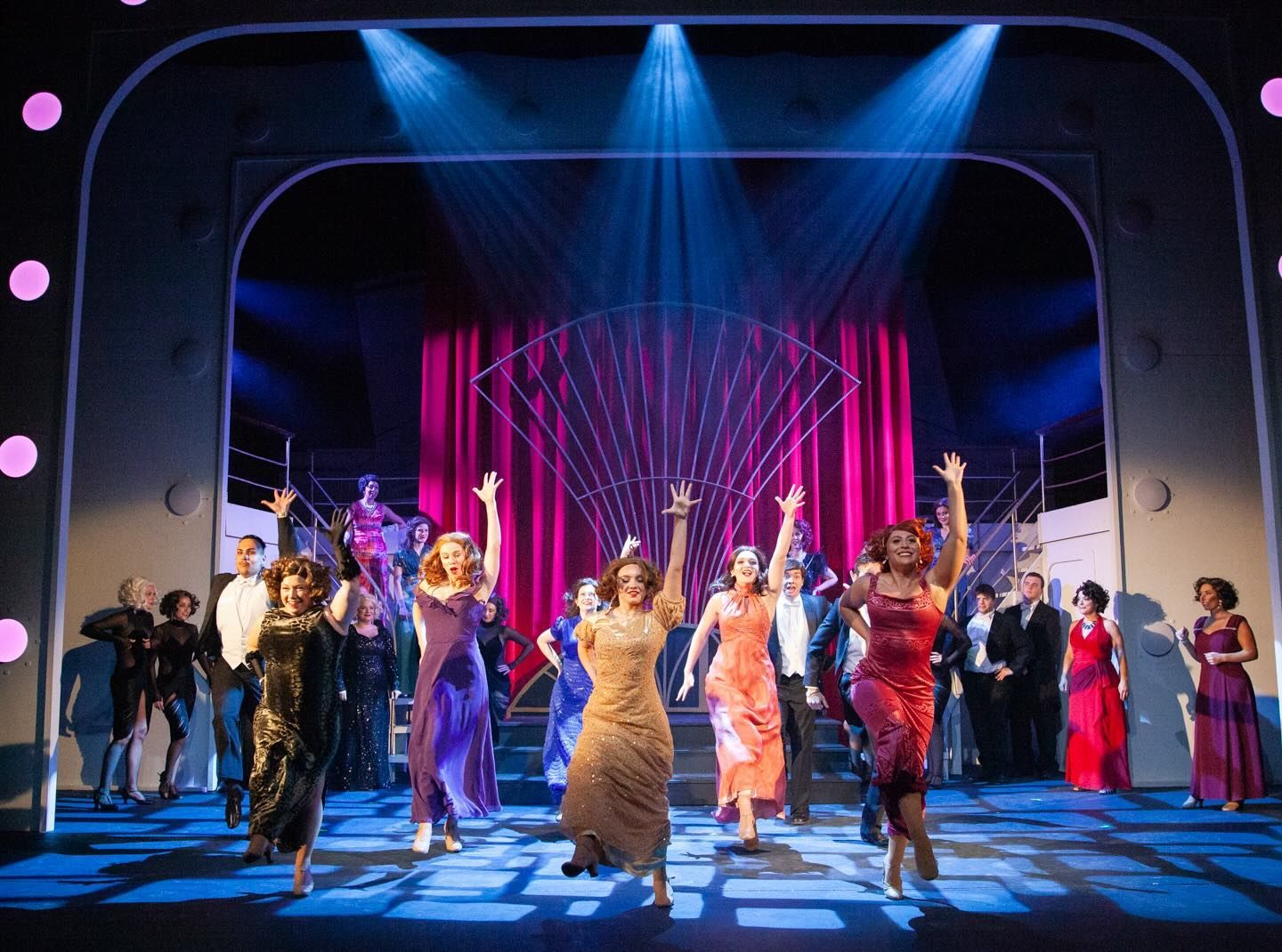 A group of people are dancing on a stage in front of a pink curtain.