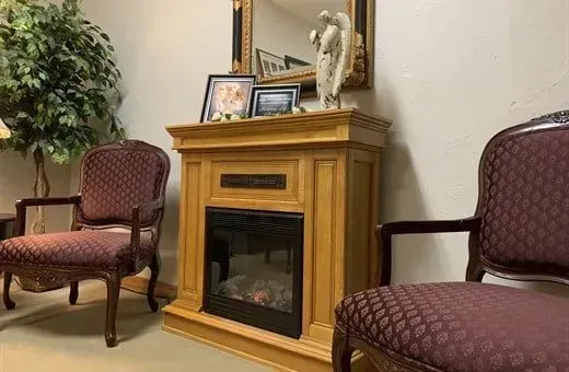 Waiting room with two patterned armchairs and a wood fireplace mantel with decor.