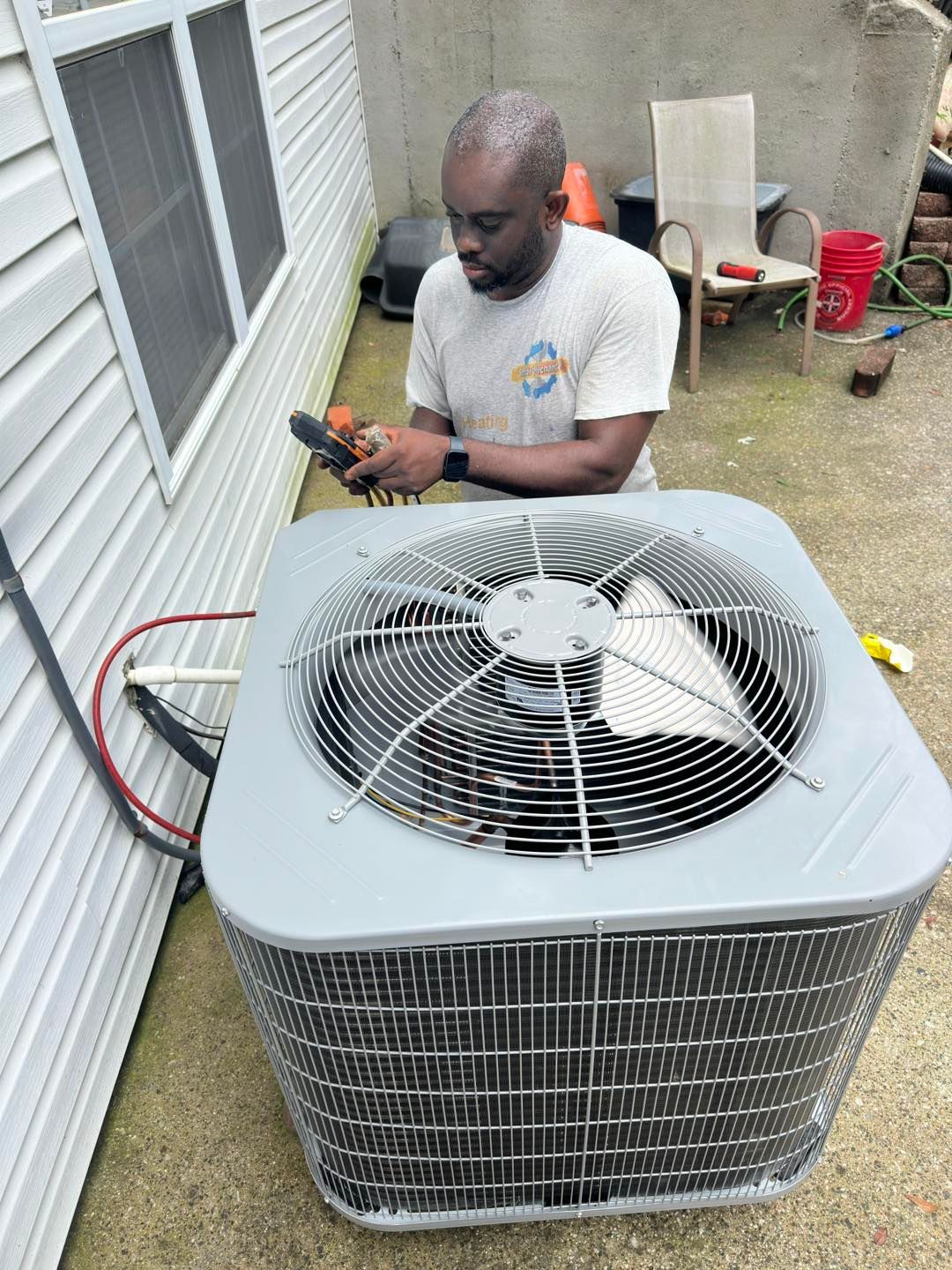 Two technicians in blue uniforms inspect an outdoor air conditioner unit with tools.