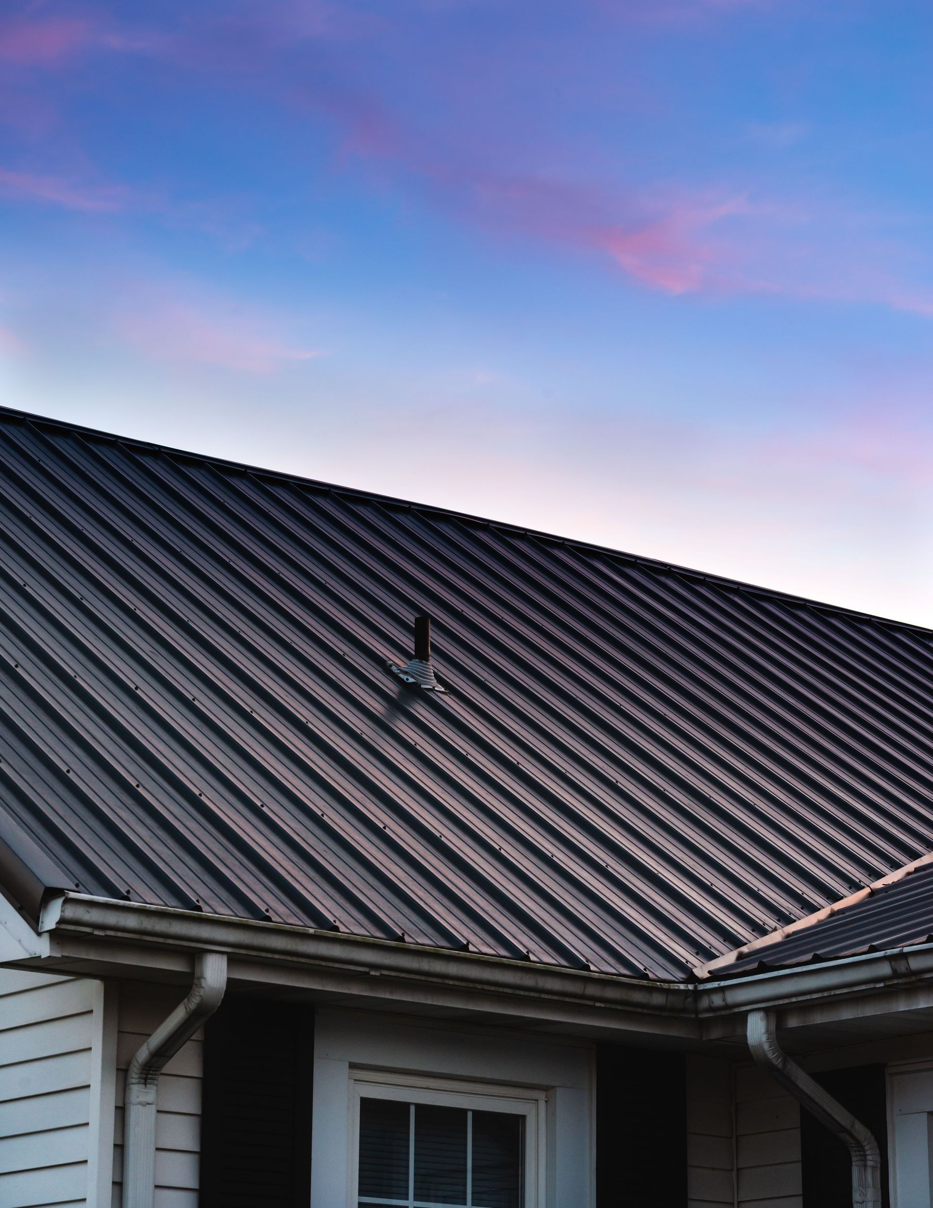 Metal roof on a white house, with a blue and pink sky above.