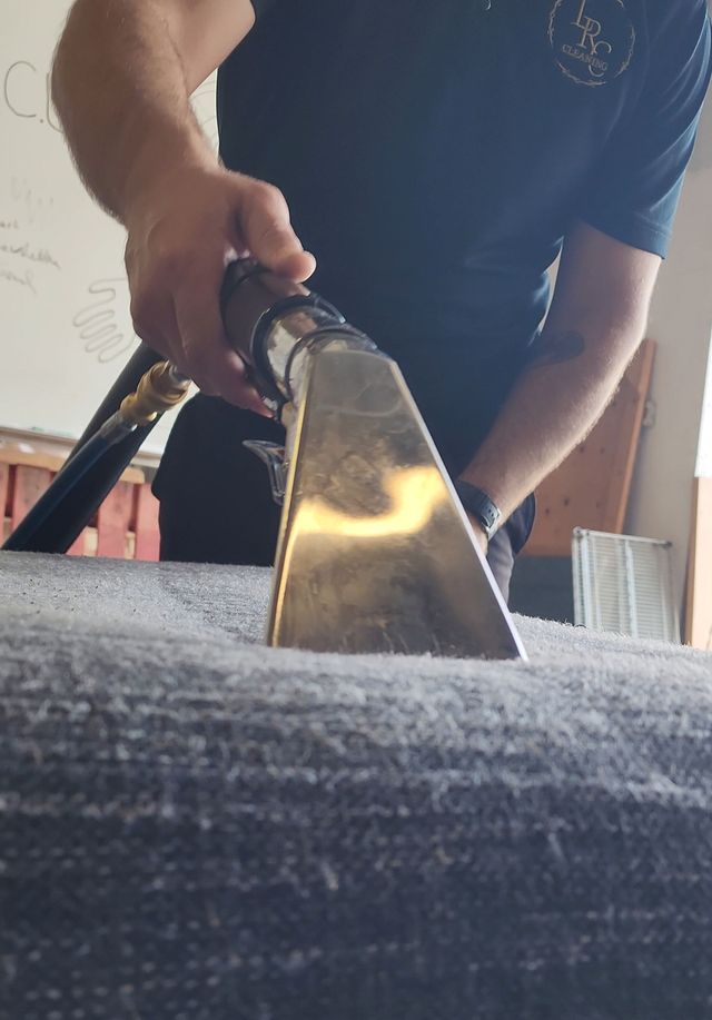 Person steam-cleaning a patterned rug with an industrial cleaner in a living room.