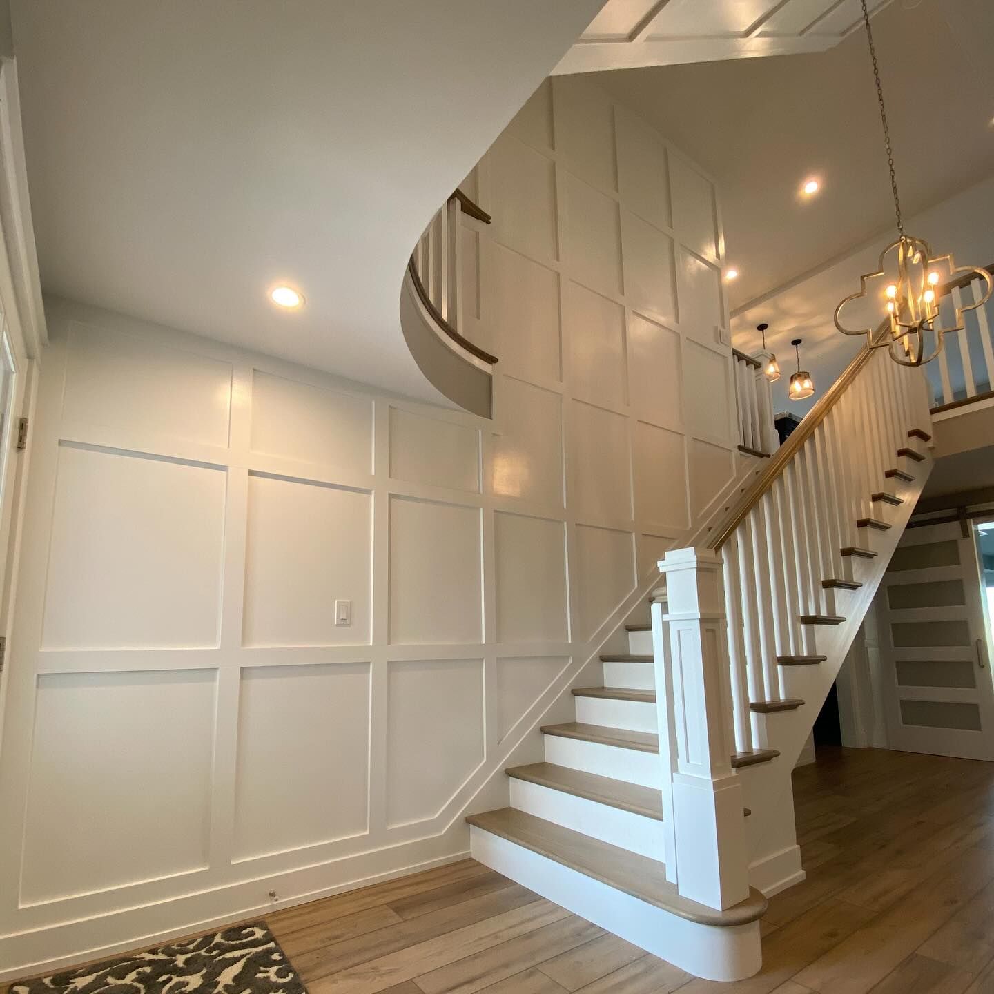 A white paneled entryway with a staircase, lit by recessed lighting, and a gold chandelier remodeled by j.k. construction llc in cape may county, new jersey