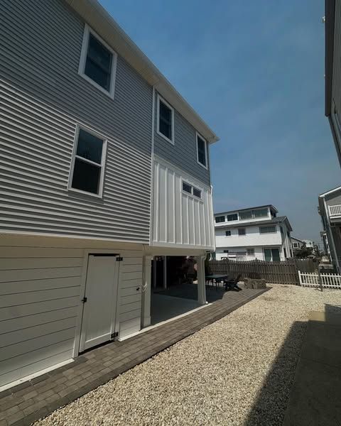newly built two-story home addition house with gray siding, white trim, and a gravel driveway in strathmere, new jersey by j.k. construction llc