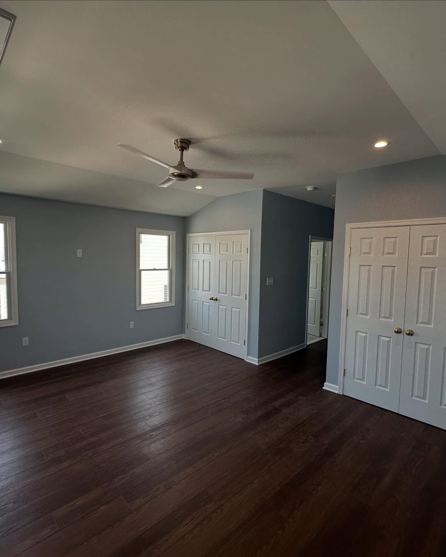newly built spacious bedroom with blue walls, dark wood floor, white closet doors, and a ceiling fan done by j.k. construction llc