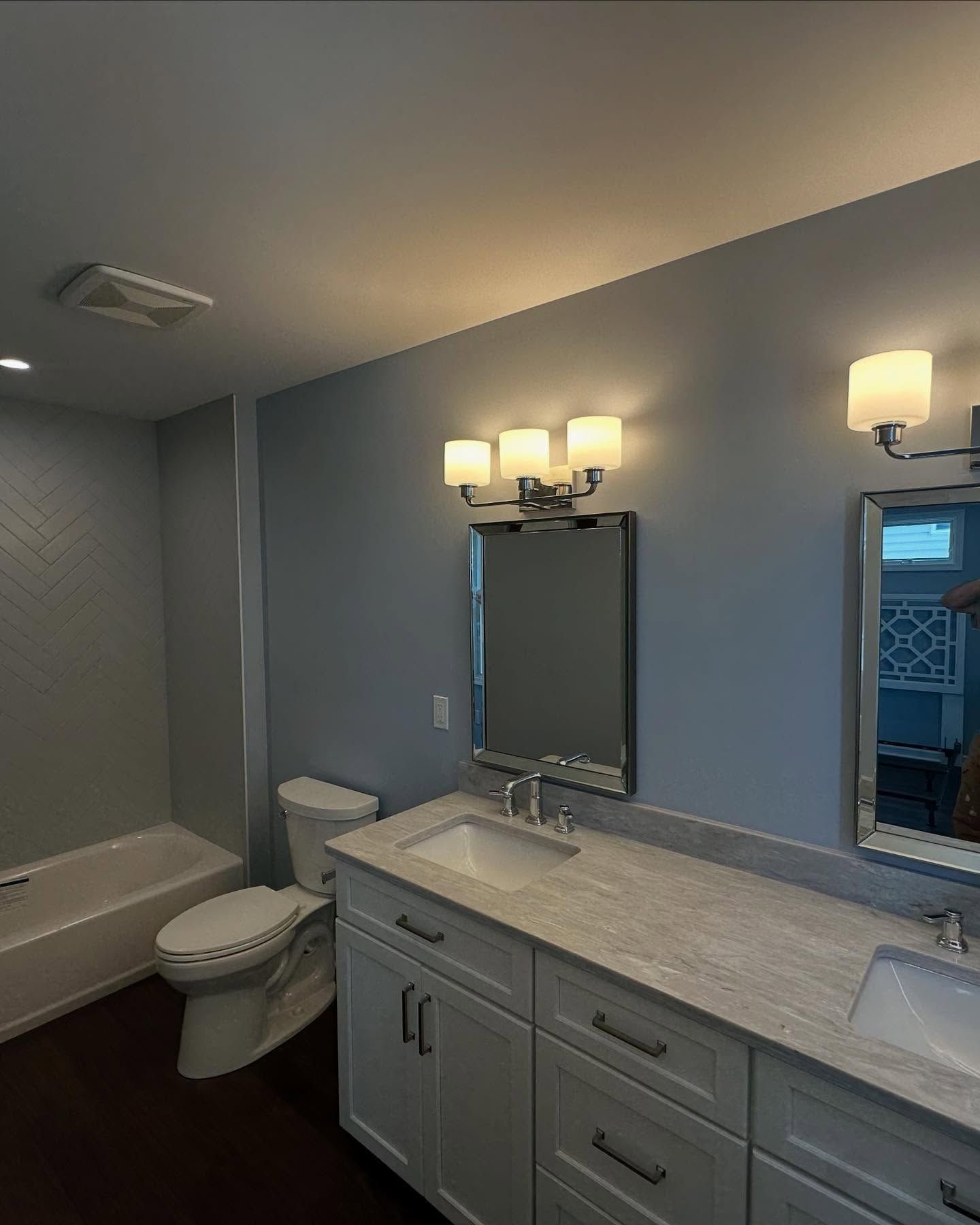 new built bathroom with blue walls, white vanity, toilet, bathtub, and silver-framed mirrors with light fixtures built by j.k. construction llc in cape may county, new jersey