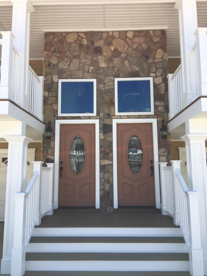 a renovation of two brown doors with oval glass insets, set in a stone wall, with white railings and a staircase done by j.k. construction llc in wildwood, new jersey