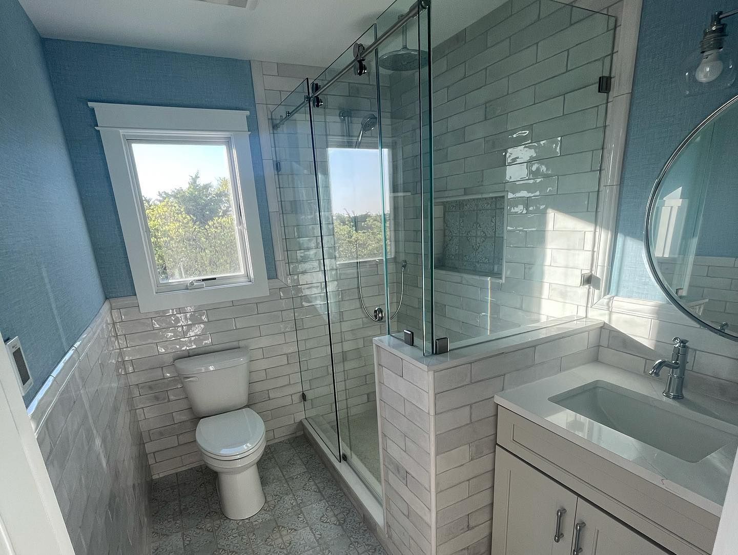 renovated, modern bathroom with a glass shower, toilet, and vanity; light blue walls, white and gray tiles in avalon, new jersey done by j.k. construction llc