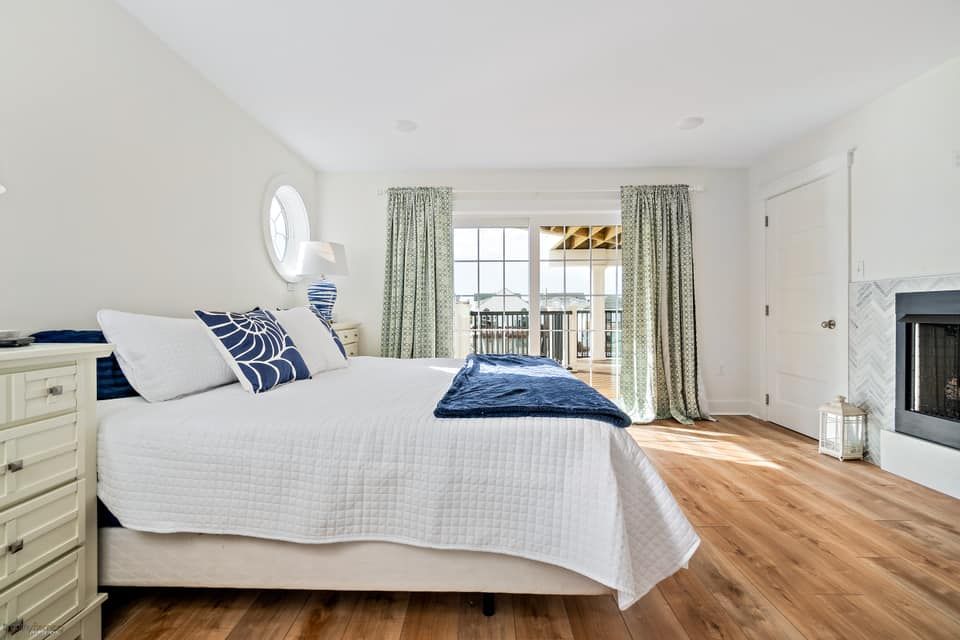 renovated open bedroom with white bed, blue accents, and balcony access; light wood floors in stone harbor, new jersey done by j.k. construction llc