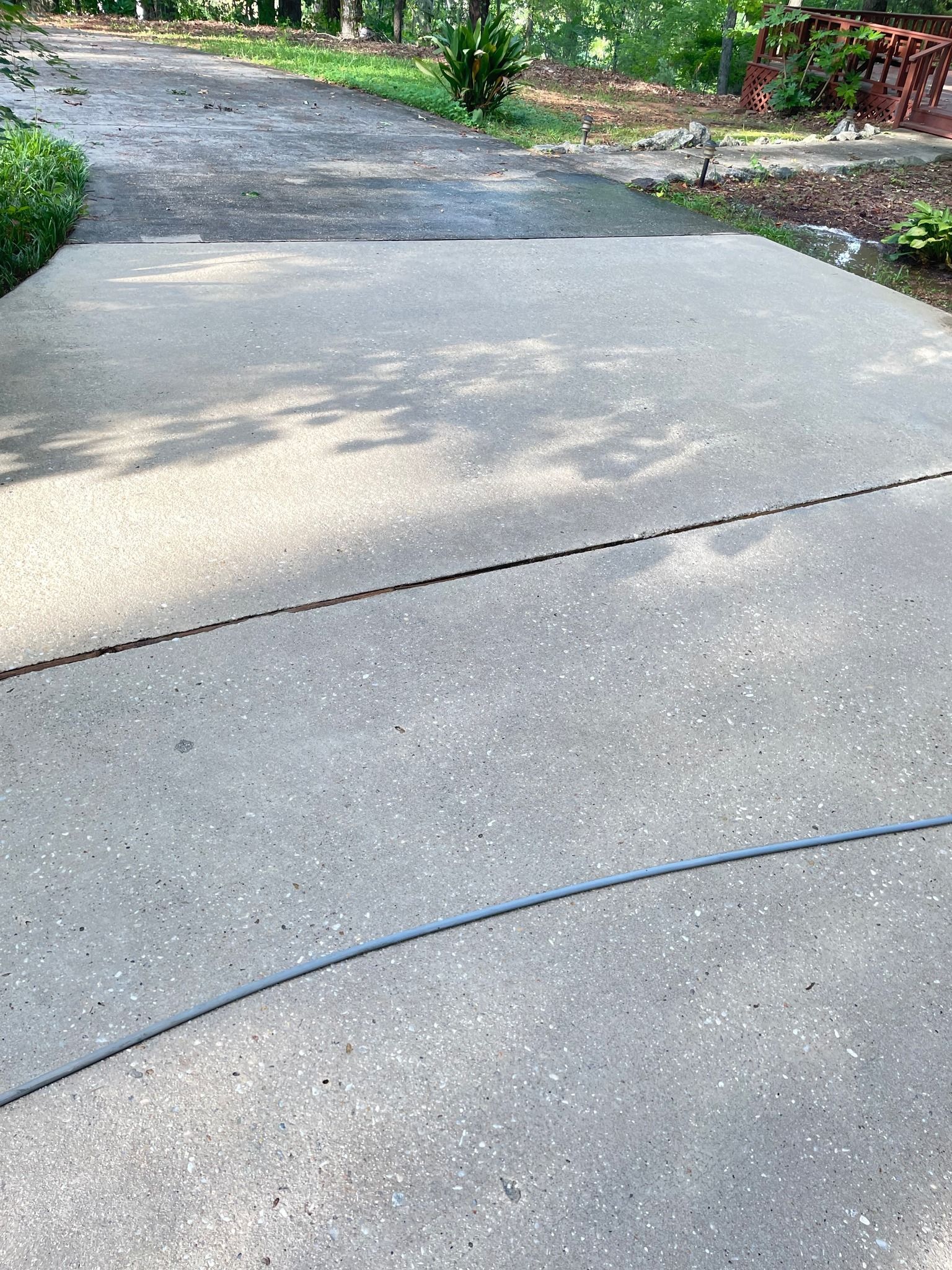 Gray concrete driveway with a black seam and blue hose.