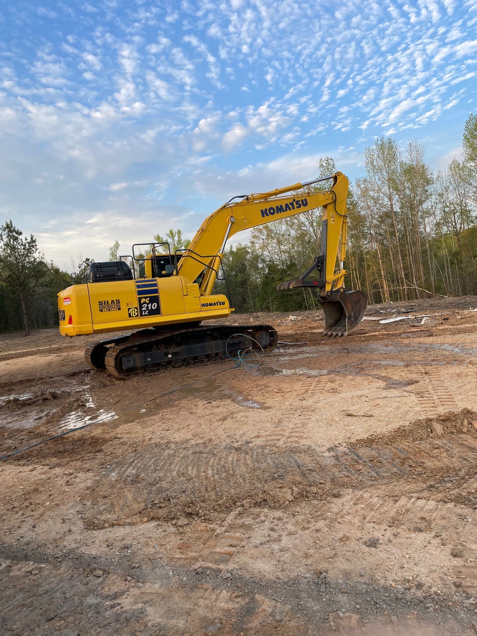 Yellow excavator on dirt, preparing a construction site under a partly cloudy blue sky.