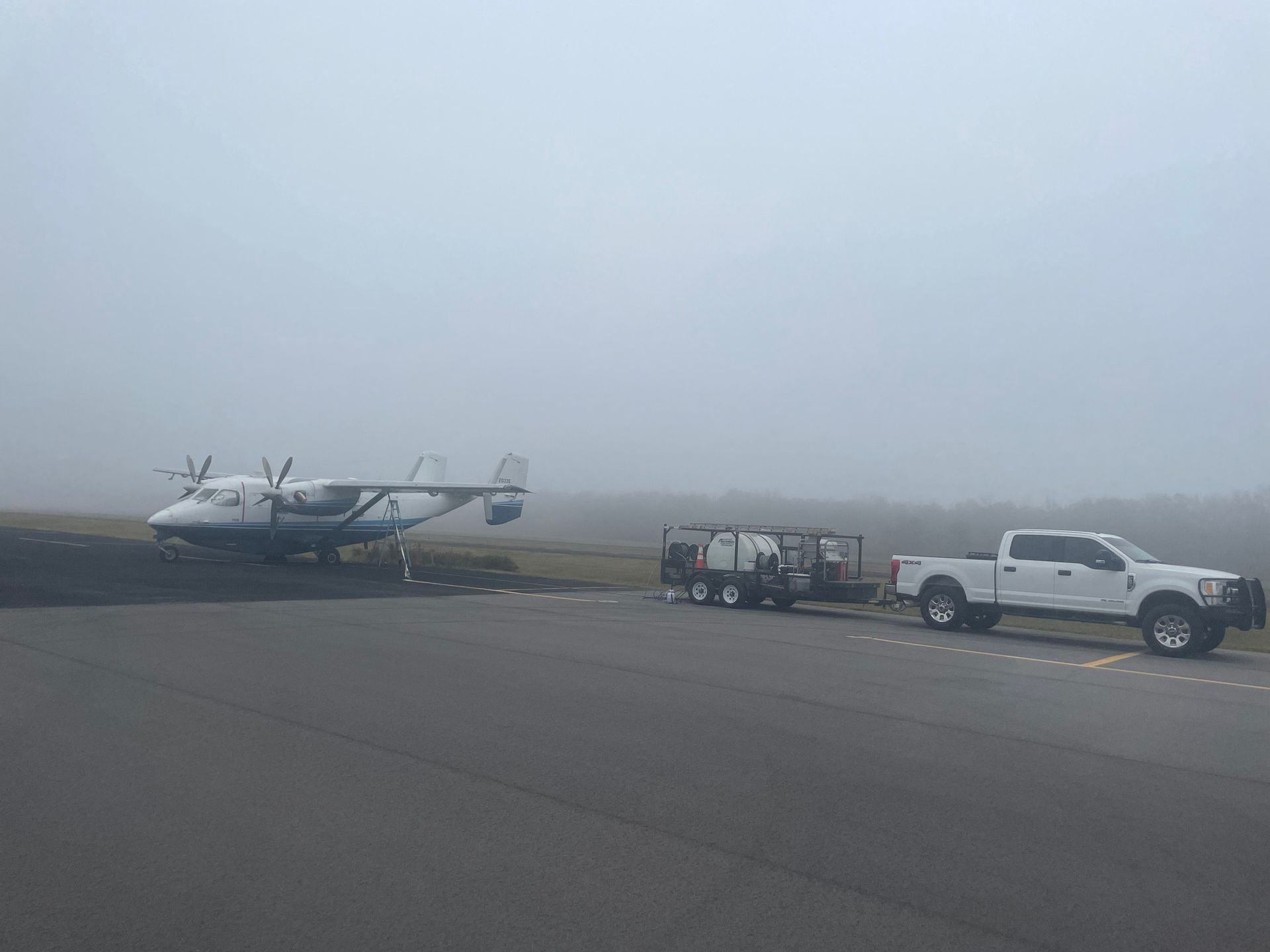 Airplane parked on a runway with a truck towing a trailer on a foggy day.